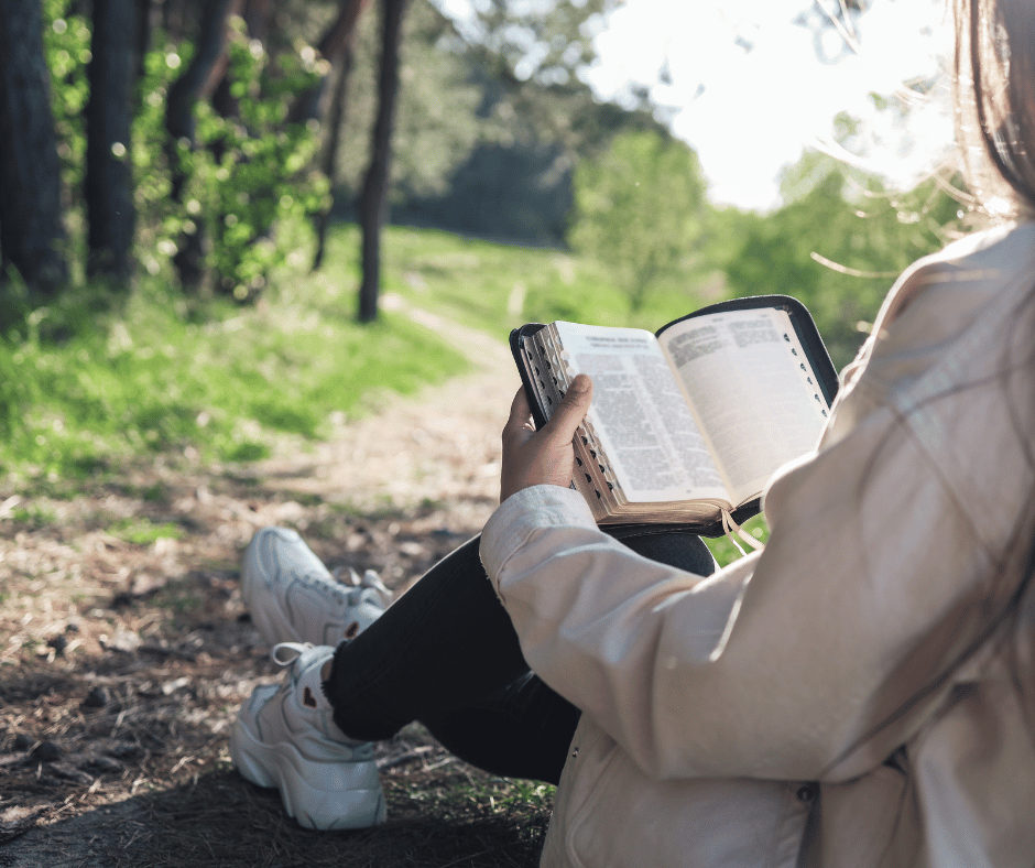 Someone sitting outside on the grass reading the bible